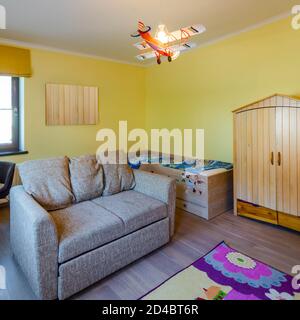 Modern interior of children`s room in apartment. Cozy furniture. Small wooden bed. Yellow walls. Wardrobe. Stock Photo